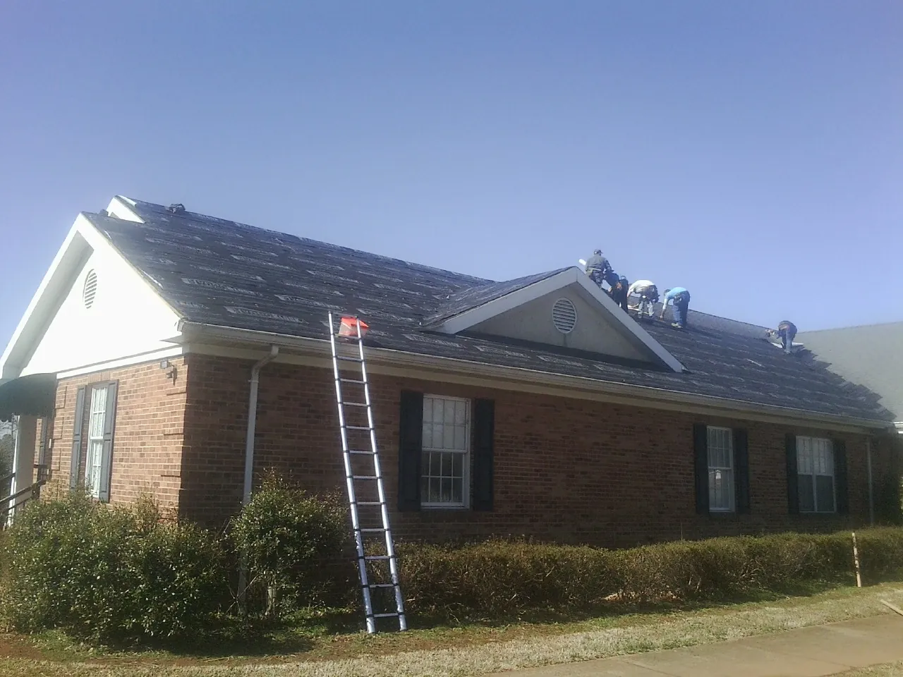 Crew tearing shingles off a brick ranch roof with a ladder set — Emergency Roof Repair work by our crew in Rhinecliff
