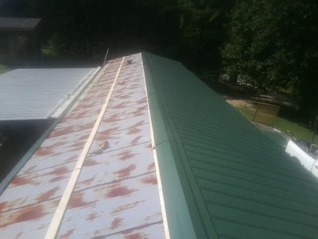 Old rusted panels beside newly installed green metal roofing — Wind Damage Roof Repair by Roofing Brothers in Rhinecliff