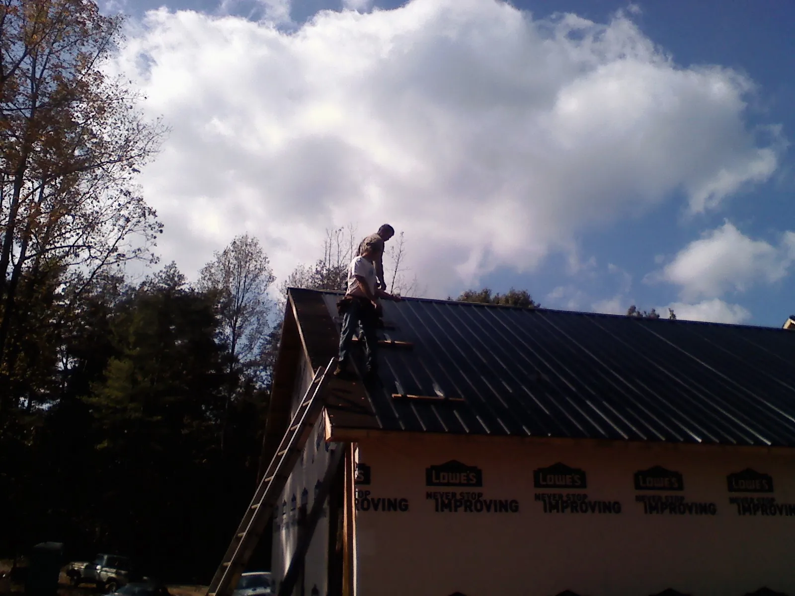 Roofer fastening dark metal panels high against a cloudy sky, from a Roof Inspection job in Rhinecliff
