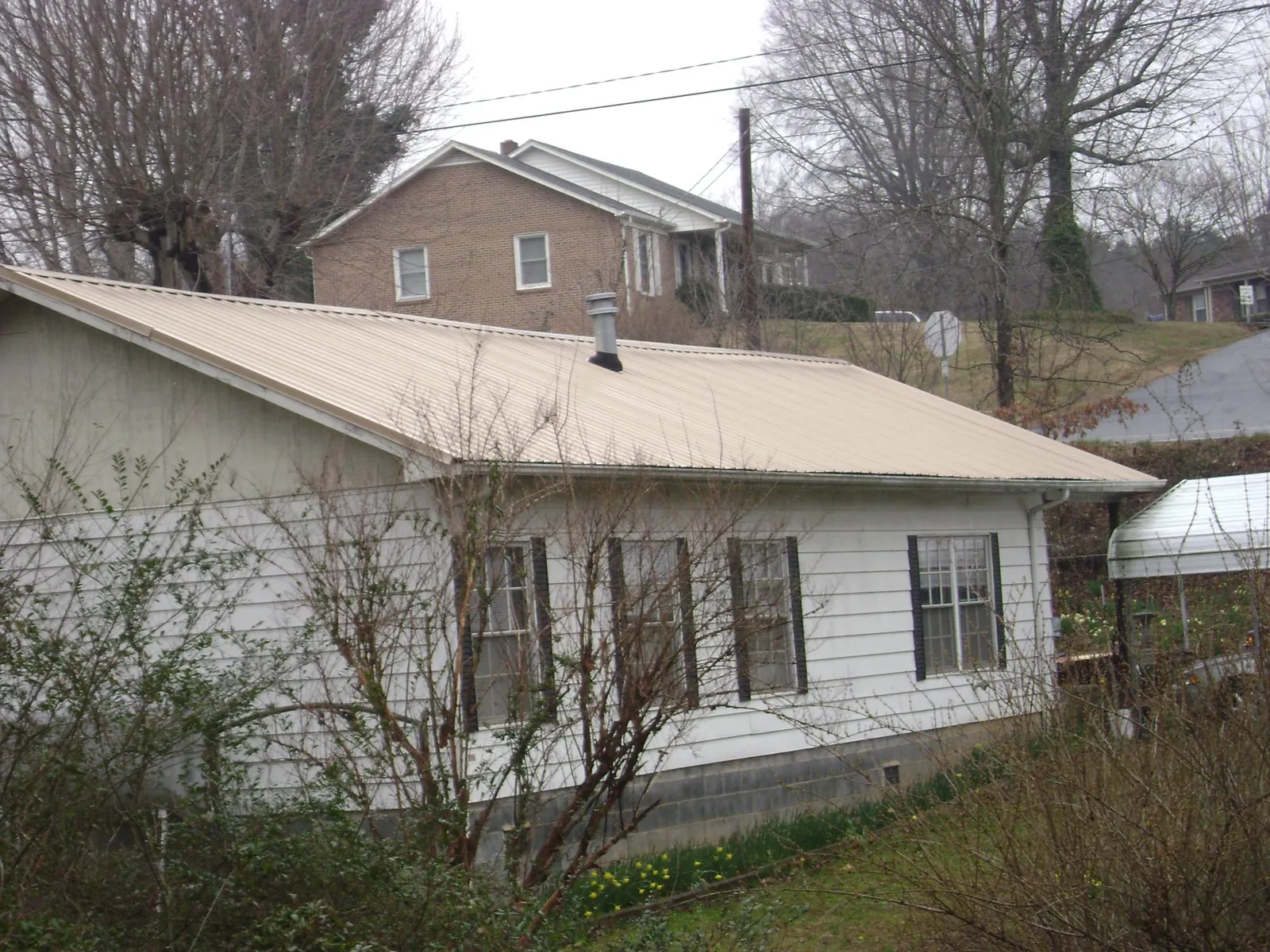 Tan metal roof on a white sided house set into a hillside — Commercial Roofing by Roofing Brothers in Rhinecliff